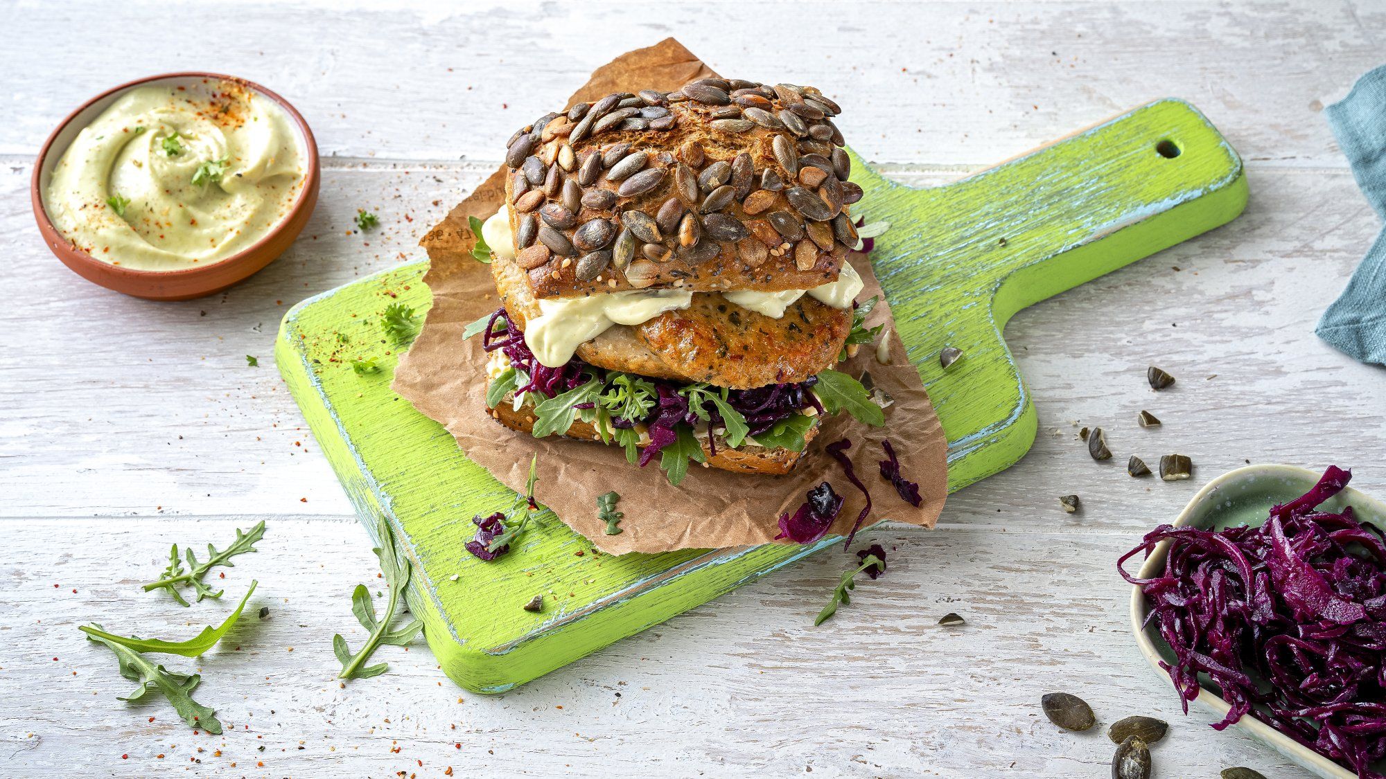 Belegtes Brötchen mit Dip in Schale serviert auf grünem Holzbrett